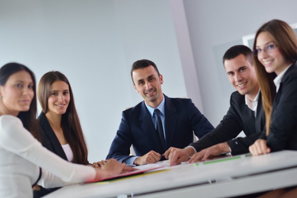 A professional team sitting around a conference table, smiling and engaged in a discussion, representing efficient employee records management.