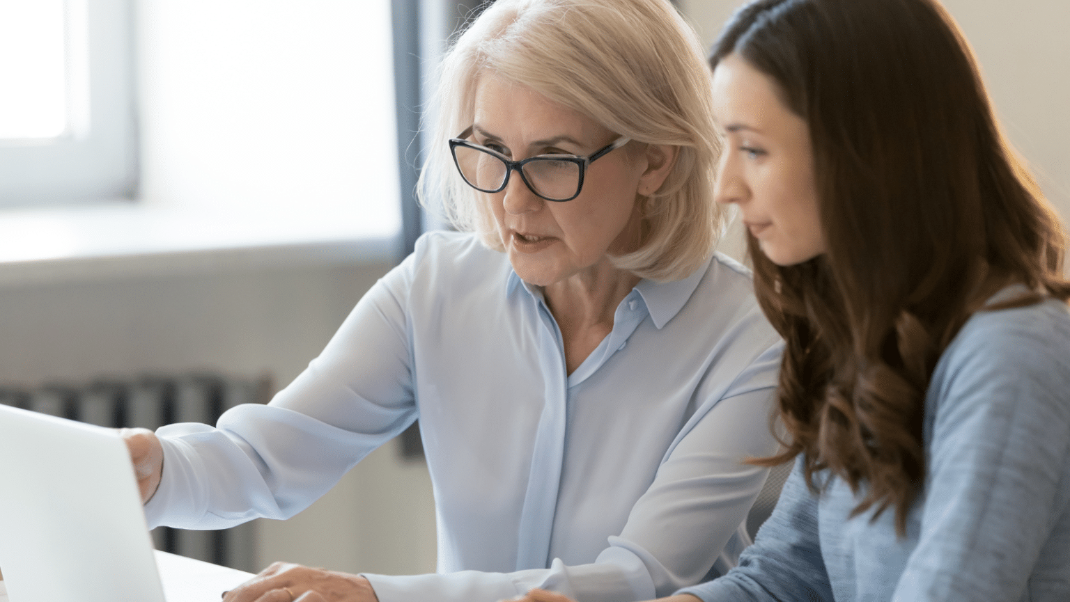 Young employee mentoring senior colleague on workplace technologies, showcasing reverse mentorship in HR