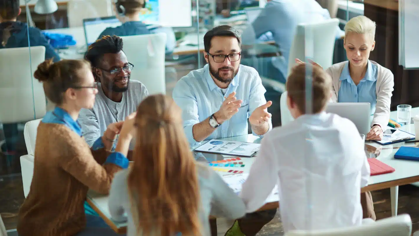 Diverse group of professionals engaged in an open team discussion during a meeting, promoting psychological safety and collaboration.
